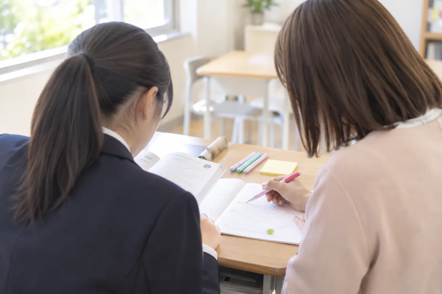 講師と生徒が並んでノートをのぞき込む授業のようす